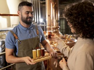 : Una persona observa una muestra de cerveza mientras le presentan otras tres en una cervecería.