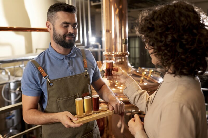 : Una persona observa una muestra de cerveza mientras le presentan otras tres en una cervecería.