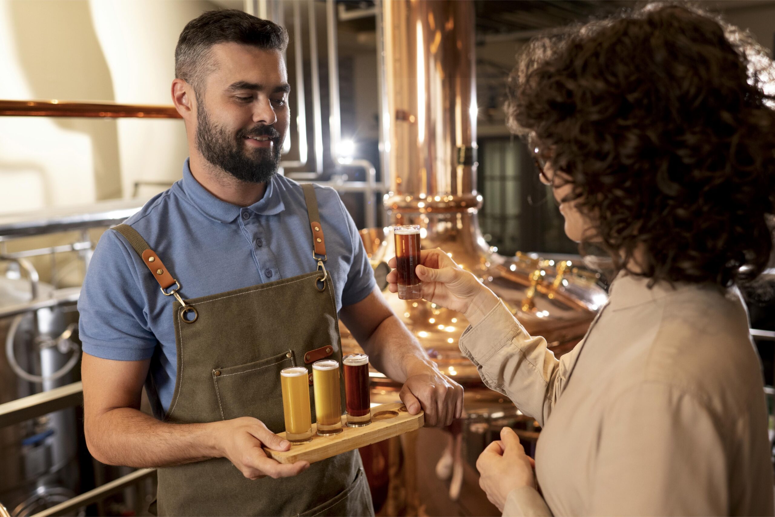 : Una persona observa una muestra de cerveza mientras le presentan otras tres en una cervecería.